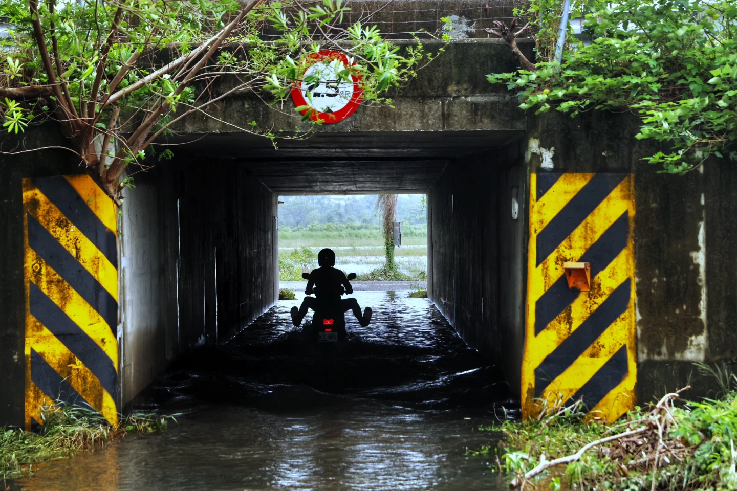 台南安定遭大雨襲擊,一處涵洞隧道積水,民眾騎摩托車涉水抬高雙腳,以免弄濕。林林攝