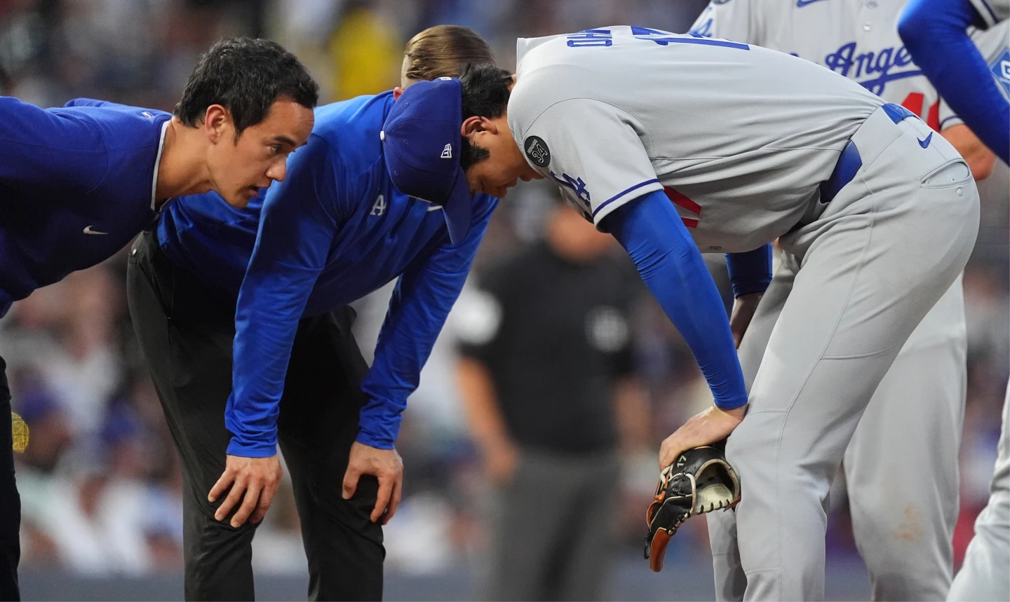 道奇隊大谷翔平在比賽中被強襲球打中右大腿,防護員、翻譯趕緊上場關心。美聯社