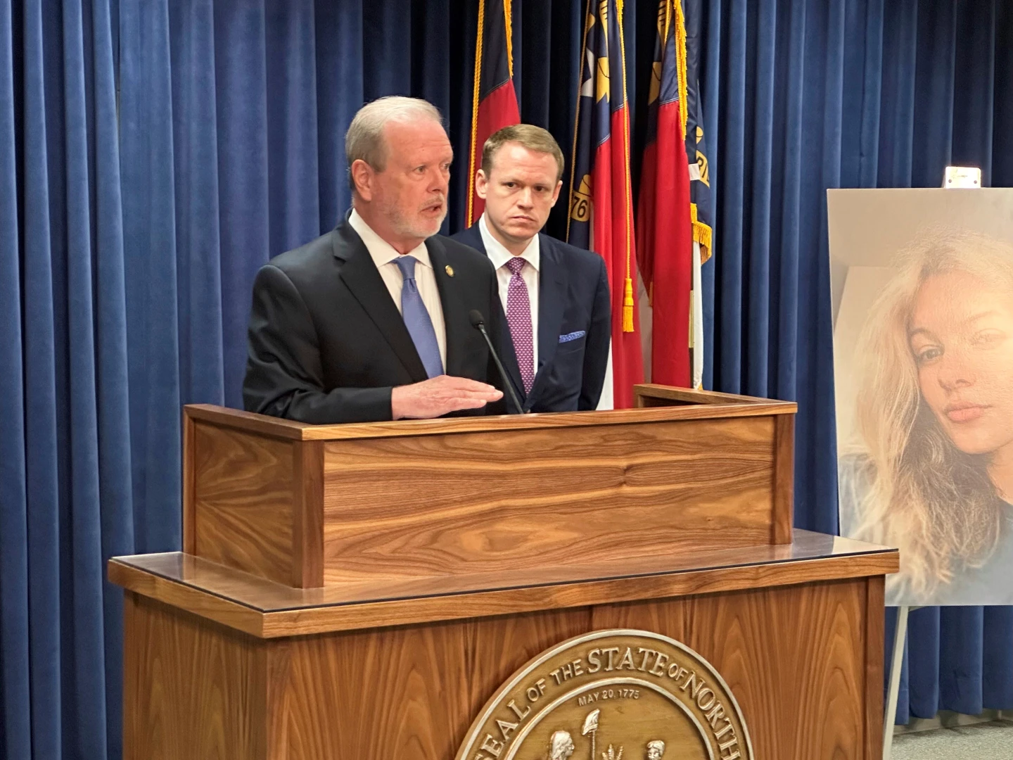 北卡羅來納州參院領袖伯杰(左前)和州議長霍爾(右後)11日表示,正推進一系列法律提案,旨在收緊庭審前釋放規則,以確保烏克蘭女難民扎魯茨卡(圖右海報)在電車遇害的類似案件再度上演。美聯社