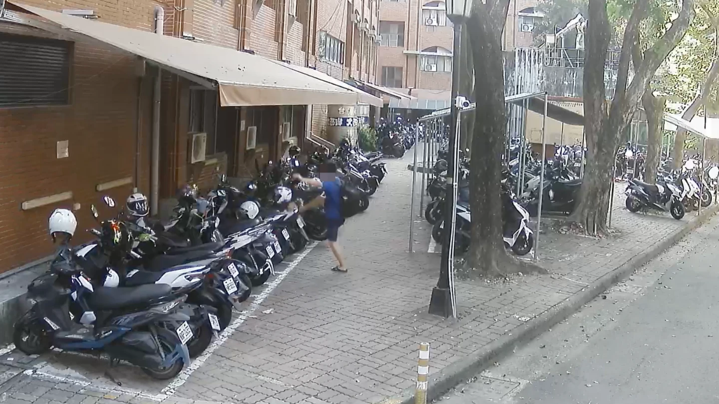 一名穿藍衣的背包男在高科大楠梓校區停車場踹倒機車。高科大提供